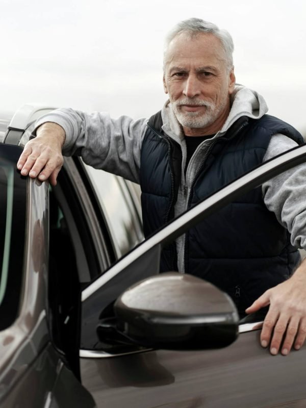 close-up-confident-senior-man-standing-by-his-new-car-in-the-outdoors-parking-lot-of-a-dealership.jpg